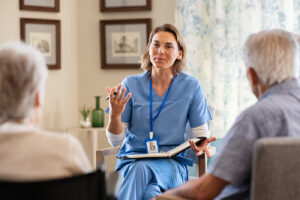 Eine Community Health Nurse sitzt bei einem Beratungsgespräch im Wohnzimmer eine älteren Ehepaars.