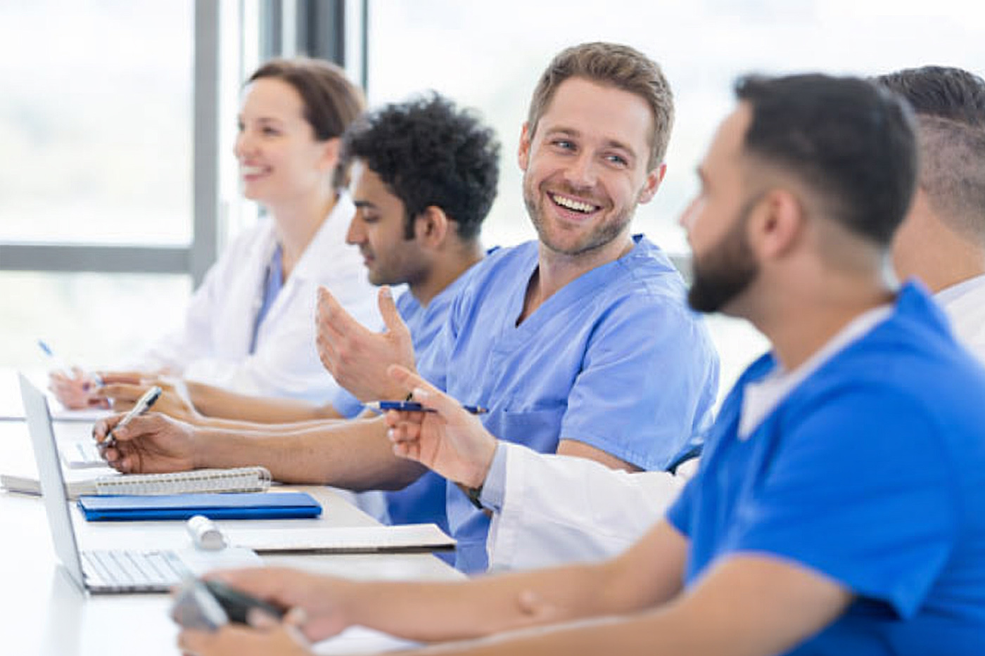 Verschiedene Pflegekräfte nehmen an einer Pflichtfortbildung in der Pflege teil und sitzen in einem Schulungsraum.