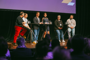 Sechs Teilnehmer einer Podiumsdiskussion stehen auf einer Bühne