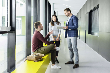 Drei Personen stehen im Flur eines Bildungsinstituts und unterhalten sich.