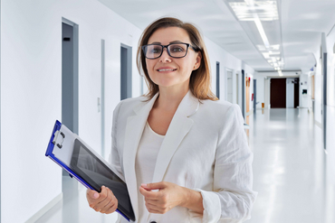 Eine Frau steht mit einem Klemmbrett in einem Krankenhausflur.