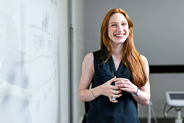 Eine Frau steht an einem Whiteboard und lächelt in die Kamera.