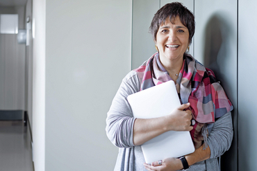 Eine Mitarbeiterin einer Klinik steht mit einem Laptop in der Hand in einem Flur.