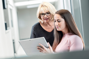 Zwei Frauen betrachten ein Tablet und unterhalten sich.