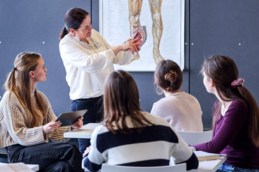 Eine Pflegepädagogin unterrichtet in einem Klassenraum und hält ein künstliches Herz in der Hand.